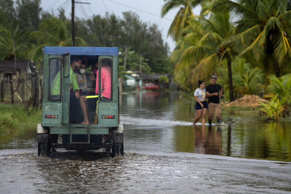 Passengers sit in the back of a vehicle as they are transported through a street flooded by rain brought on by Hurricane Ida, in Guanimar, Artemisa province, Cuba, Saturday Aug. 28, 2021. (AP Photo/Ramon Espinosa)