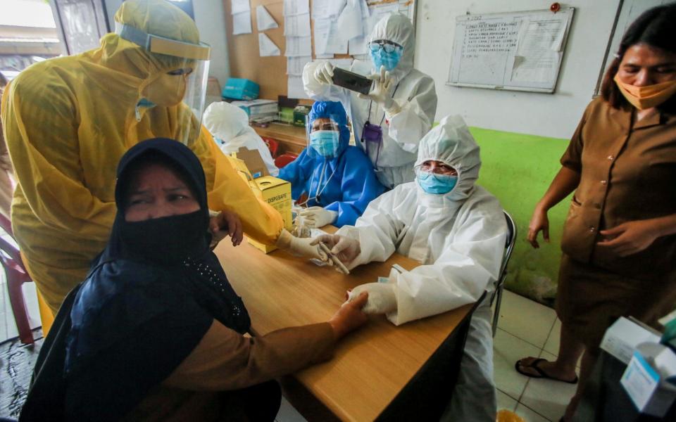 Healthcare workers clad with hazmat suits collect blood samples from a women during an antibody rapid test for coronavirus in Medan, North Sumatra, Indonesia - Dedi Sinuhaji/EPA-EFE/Shutterstock