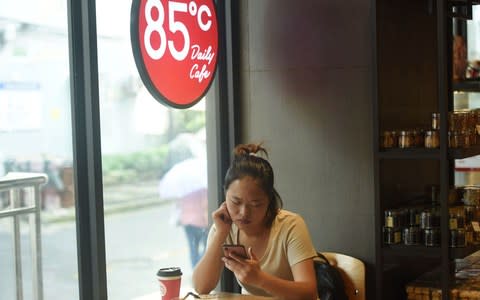 A woman looks at her mobile phone at a 85C Bakery Cafe in Hangzhou in China's eastern Zhejiang province - Credit: AFP