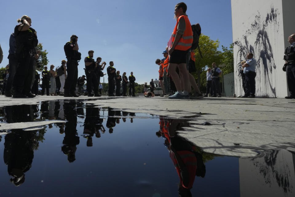 FILE - Police officers guard climate activists with the group Uprising of the Last Generation after they threw black paint on the wall of the chancellery in Berlin, Germany, June 22, 2022. The group claims the world has only a few years left to turn the wheel around and avoid catastrophic levels of global warming. (AP Photo/Markus Schreiber, File)