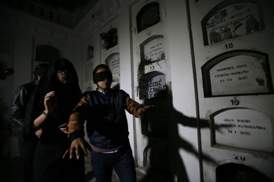 Blindfolded tourists walk through El Tejar cemetery, in downtown Quito, Ecuador, Wednesday, Sept. 11, 2019. They're there to get a taste of death while still alive, spending part of the night in a dark crypt at the El Tejar cemetery, the latest example of the so-called "necro tourism" trend luring those with a keenness for the macabre. (AP Photo/Dolores Ochoa)