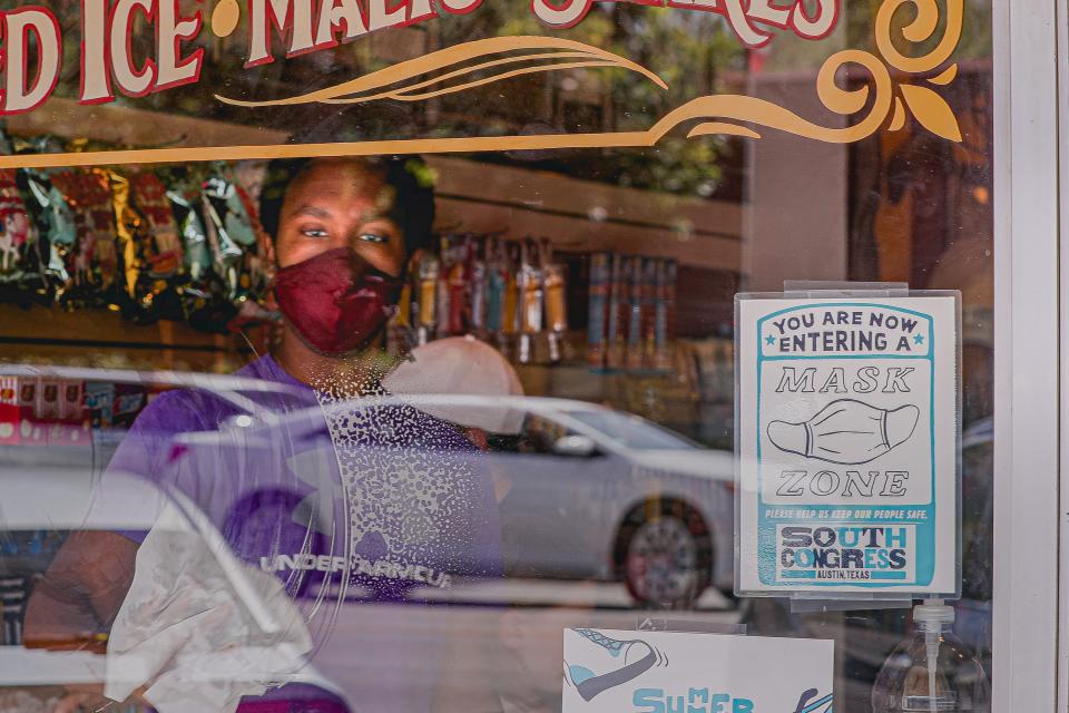 A store employee wearing a mask cleans a window with a sign requesting customers put on masks at a shop on South Congress Avenue. Travis County in Texas moved back to Stage 4 of COVID rules and health officials are asking residents who have yet to receive a coronavirus vaccine to sign up for one immediately.