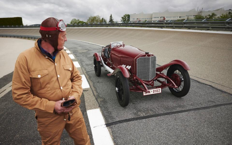 Andrew English in 1920s motoring overalls stood next to the Targa Florio on the track