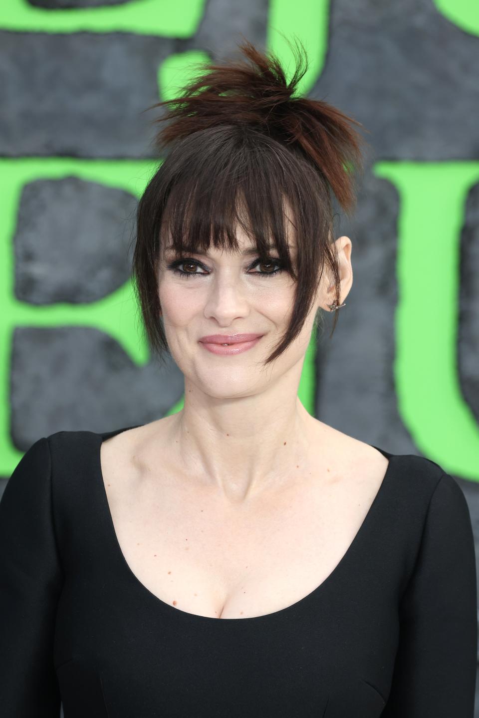 Winona Ryder in a chic black dress with a high neckline and a messy updo smiles at a TV and film event