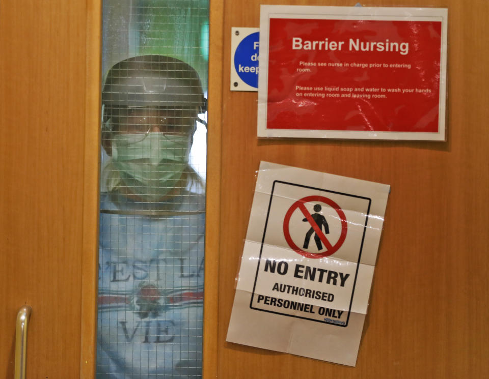 A nurse wearing PPE looks through a window of a closed door leading to the red zone at the Wren Hall care home in Nottingham, Monday, April 20, 2020. AP visited a care home in Nottingham where 10 of their 54 residents have succumbed to COVID-19. Leading British charities said the new coronavirus is causing "devastation" in the country's nursing homes, as official statistics show that hundreds more people with COVID-19 have died than are recorded in the U.K. government's daily tally.(AP Photo/Frank Augstein)