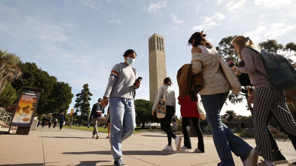 People walk on a campus with tall, thin tower in the background.