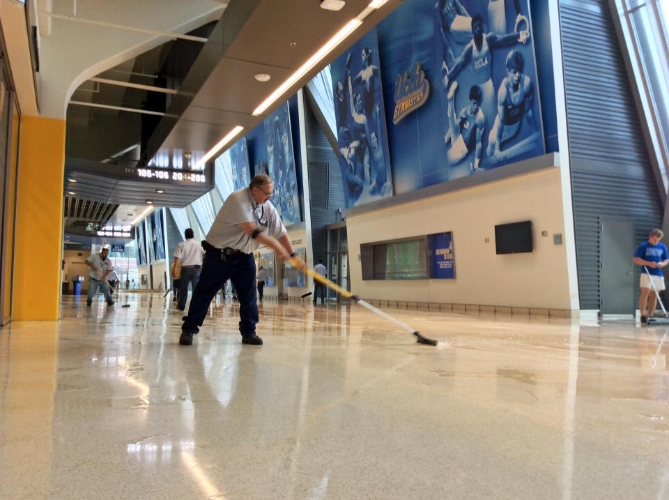 A worker clears water from the lobby floor of Pauley Pavilion, home of UCLA basketball, after a 30-inch water main burst on nearby Sunset Boulevard Tuesday, July 29, 2014, in Loss Angeles. Water also reached the playing floor of the basketball arena. (AP Photo/Matt Hamilton)