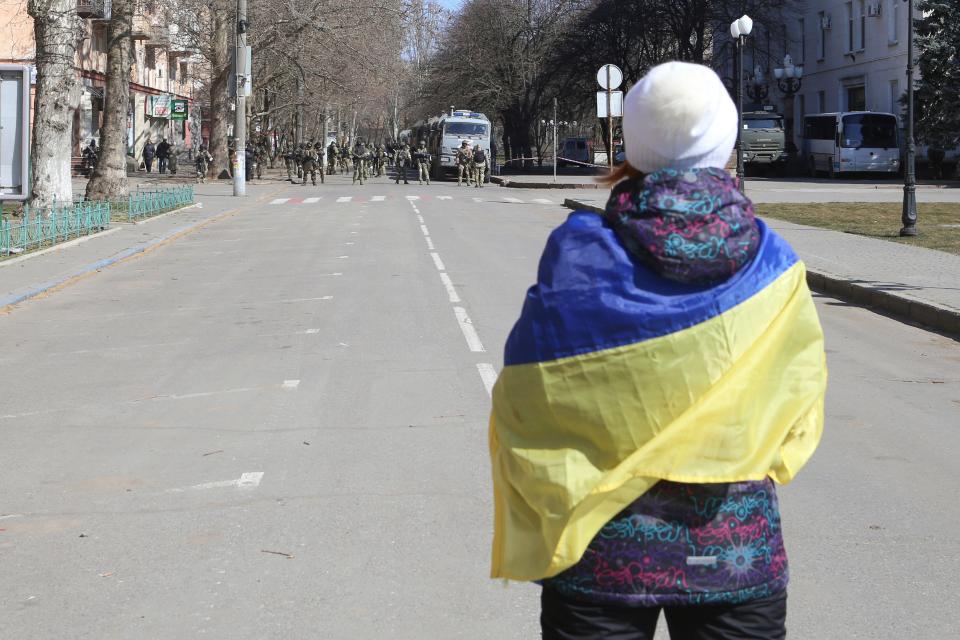 A woman wrapped in a Ukrainian flag stands in front of Russian troops during a rally against Russian occupation in Kherson, Ukraine, on March 19.