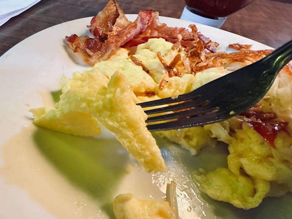 Fork picking up piece of Denny's eggs on white plate