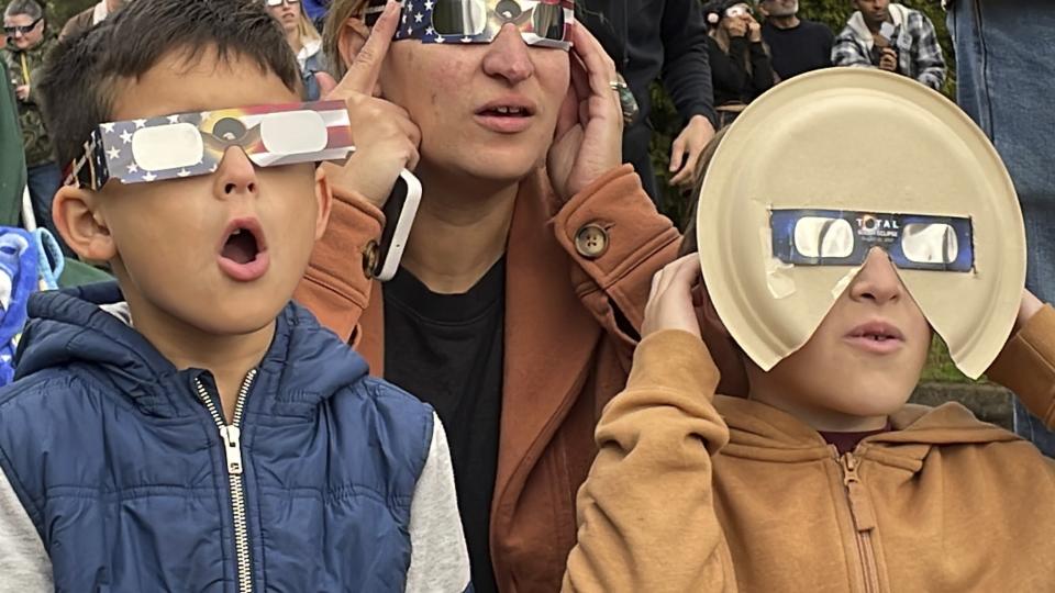 Samia Harboe, her son Logan and her friend's son wear eclipse glasses during totality of the annular solar eclipse in Eugene, Ore., on Saturday, Oct. 14, 2023. Her family came with glasses they'd made for the 2017 total eclipse and said they were excited to see another one. (AP Photo/Claire Rush)