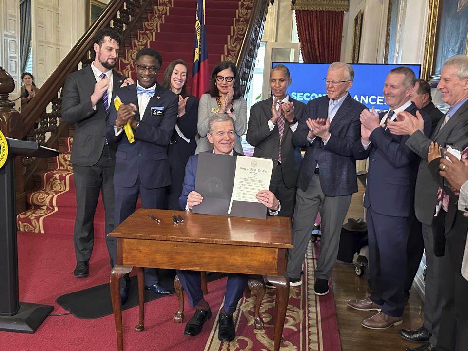 North Carolina Gov. Roy Cooper, seated, shows an executive order directing state government agencies to boost efforts at successful prisoner reentry that he signed at a ceremony at the Executive Mansion in Raleigh, N.C., on Monday, Jan. 29, 2024. (AP Photo/Gary D. Robertson)