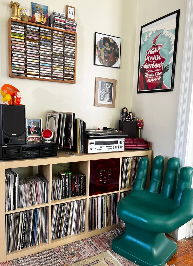 Corner view of record room with hand-shaped chair, record player, album organizer, and wall art.