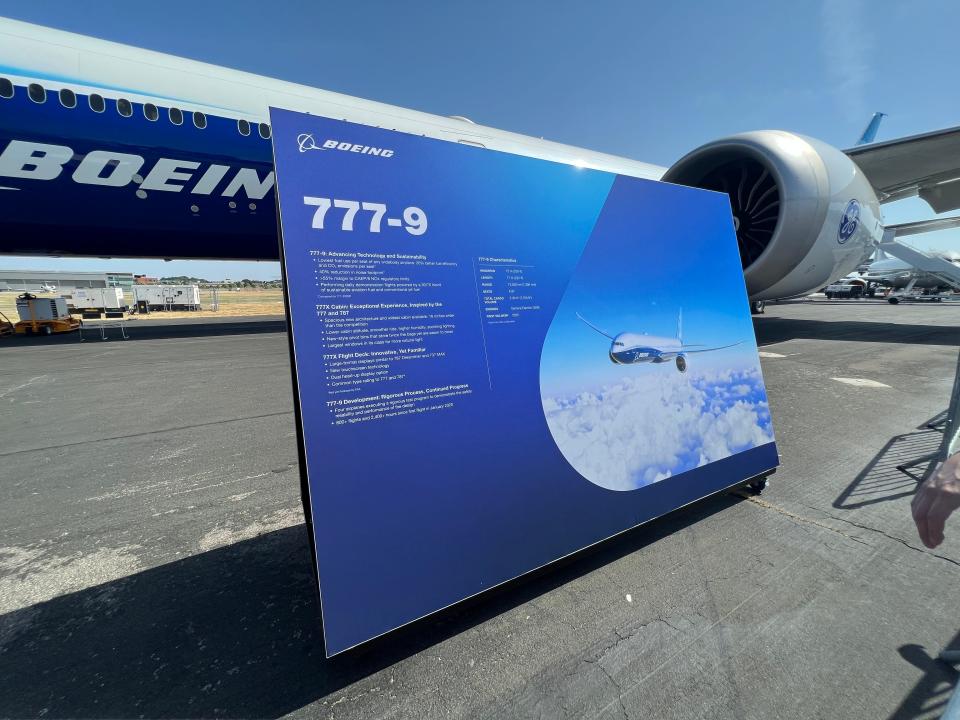 The 777x sign in front of the blue and white livery plane.