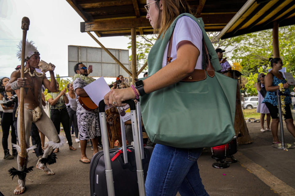 A tourist walks past a Rapanui dancer welcoming arrivals at the Mataveri airport in Hanga Roa, Rapa Nui, or Easter Island, Chile, Sunday, Nov. 28, 2022. Rapa Nui reopened after COVID-19 restrictions from March 2020 to August 2022 kept foreigners away from the island which depends 80% on tourism for its economy. (AP Photo/Esteban Felix)