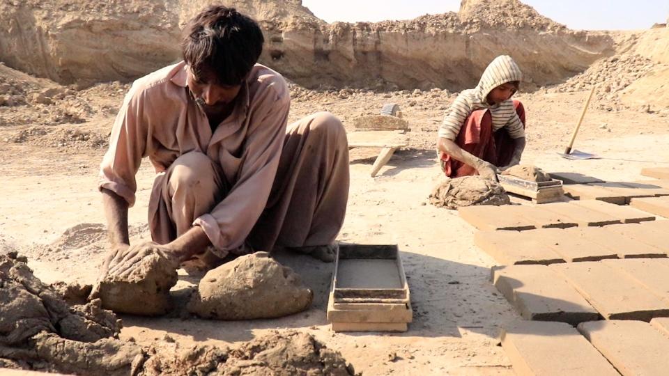 Workers loading clay into mold for brick making