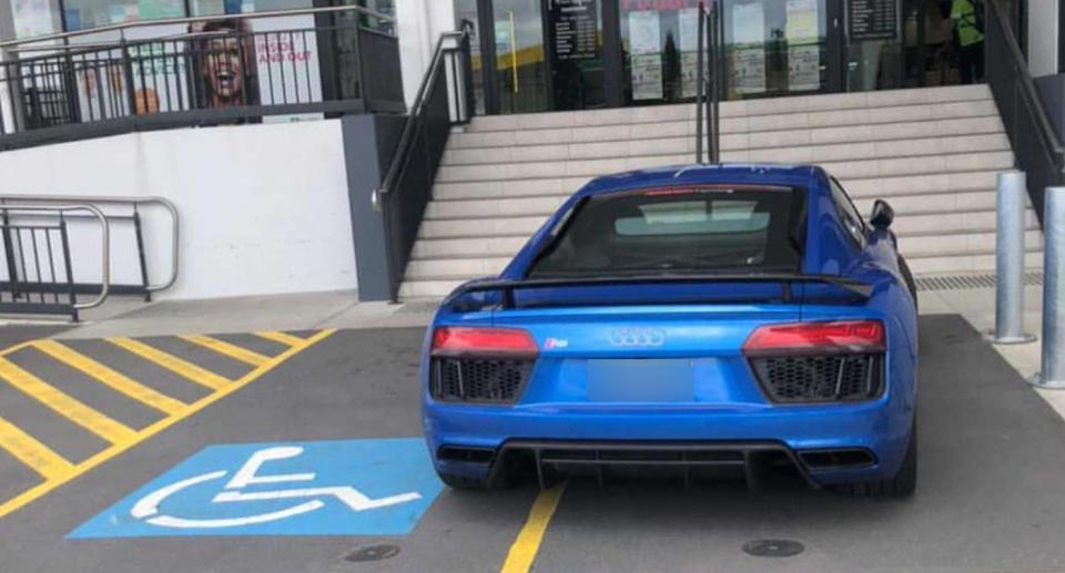 Photo shows a blue Audi parked partially over a disabled parking spot.