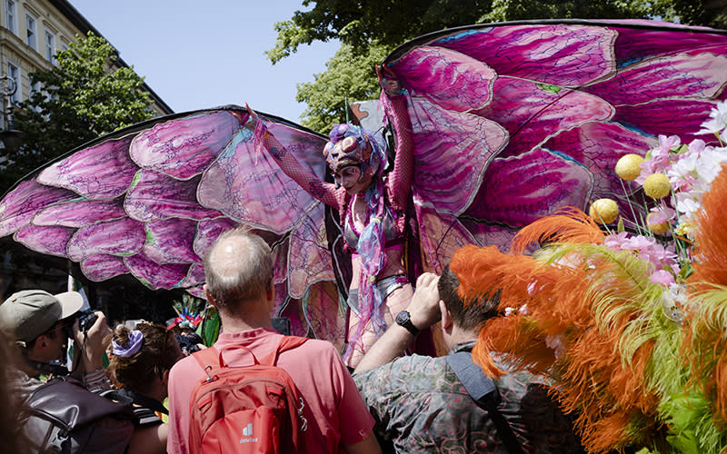 A dancer dressed in magenta spreads her costume's wings as she poses for photos before the May 28 Carnival of Cultures parade