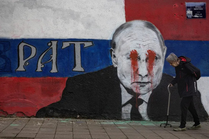 A person walks next to a mural of Russian President Vladimir Putin, which has been vandalised with red spray paint and the word 