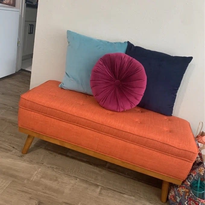 An orange bench with pink, navy and blue pillows in a reviewer's home