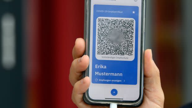 a hand holds an iphone displaying a QR code reading text in German. It is a vaccination certificate