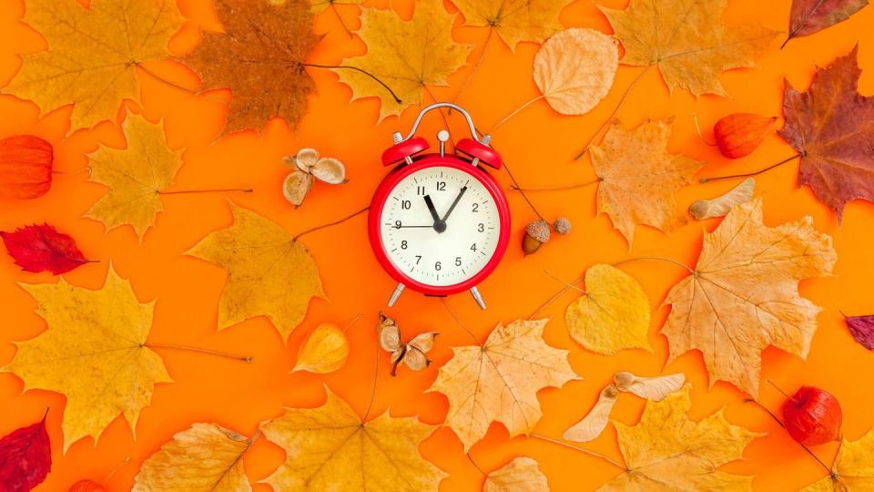 autumn postcard with fall leaves and alarm clock
