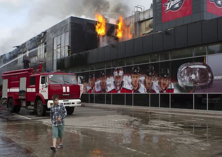 A boy walks by as firefighters attempt to extinguish a fire at the sports arena "Druzhba" (Friendship), which is the home venue of the ice hockey club "Donbass", in Donetsk, May 27, 2014. An armed group broke into the stadium in the early hours of May 27, set it on fire and left taking along some property of the stadium with them, according to local media. REUTERS/Stringer (UKRAINE - Tags: DISASTER SPORT ICE HOCKEY CIVIL UNREST) - RTR3R0AK