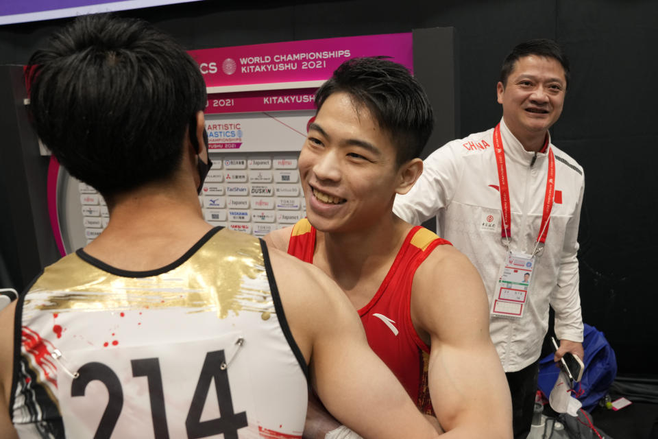 Hu Xuwei, center, of China, is congratulated by Kohel Uchimura, of Japan, after winning the horizontal bar final of the FIG Artistic Gymnastics World Championships in Kitakyushu, western Japan, Sunday, Oct. 24, 2021. Hu's coach Zheng Hao at right. (AP Photo/Hiro Komae)