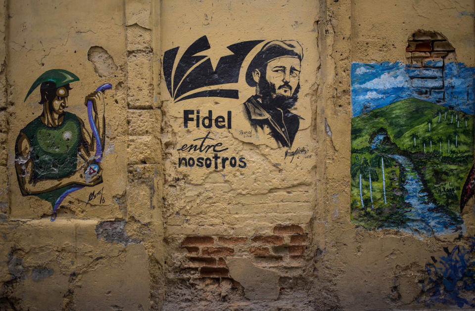 In this Aug. 13, 2018 photo, she Spanish message: "Fidel is among us" covers a wall next to an image of the late leader in Havana, Cuba. Cuba's new constitution is being debated among citizens until Nov. 15, and any revisions accepted by the government will be included in the final document to be presented in a referendum in 2019. (AP Photo/Desmond Boylan)