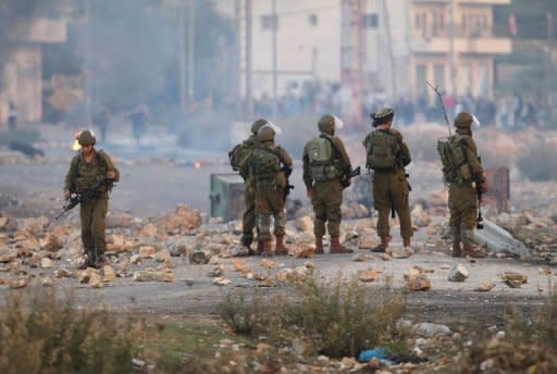 Israeli soldiers watch with Palestinian students from Birzeit University in the West Bank protest against the ongoing Israeli offensive on the Gaza Strip November 18, 2012