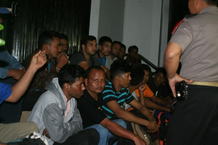 This picture taken on September 23, 2015 shows an Indonesian policeman (R) standing next to a group of migrant people at an immigration office in Sukabumi. Indonesian police have arrested 18 migrants who were stranded in the waters off Java island after their boat ran out of fuel as they tried to reach Australia, an official said. AFP PHOTO