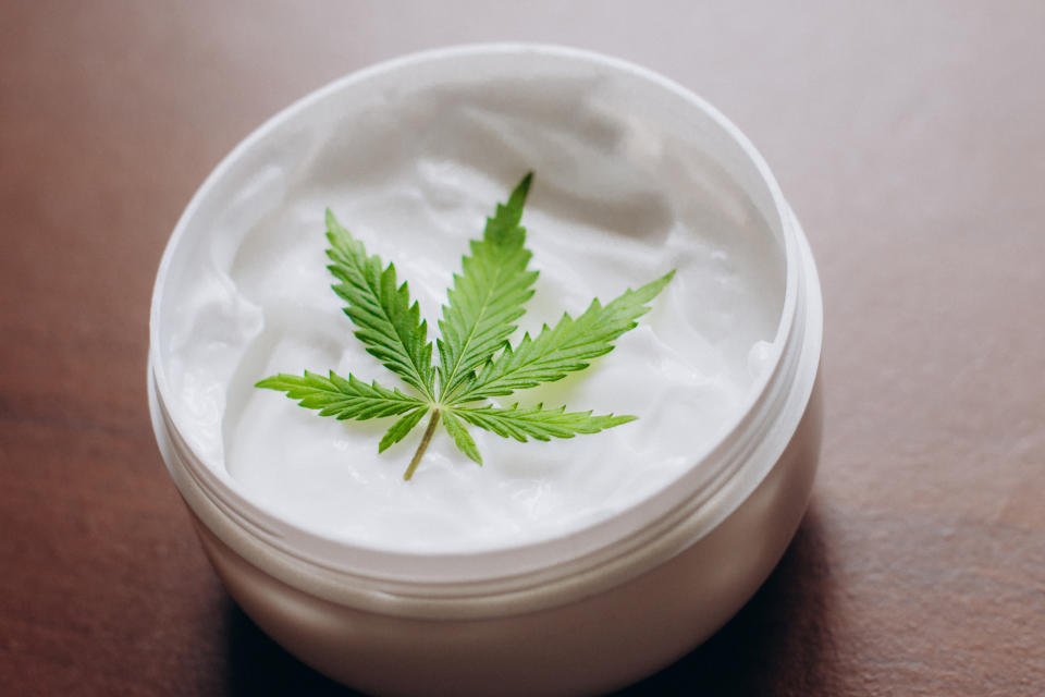 A cannabis leaf on top of an open container of topical cream