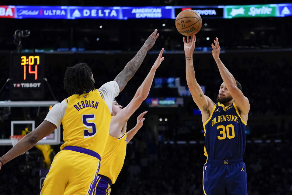 Golden State Warriors guard Stephen Curry, right, shoots againstLos Angeles Lakers forward Cam Reddish, left, and guard Austin Reaves during the first half of an NBA basketball game Tuesday, April 9, 2024, in Los Angeles. (AP Photo/Ryan Sun)