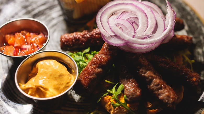 Ćevapi on a platter with onion and condiments