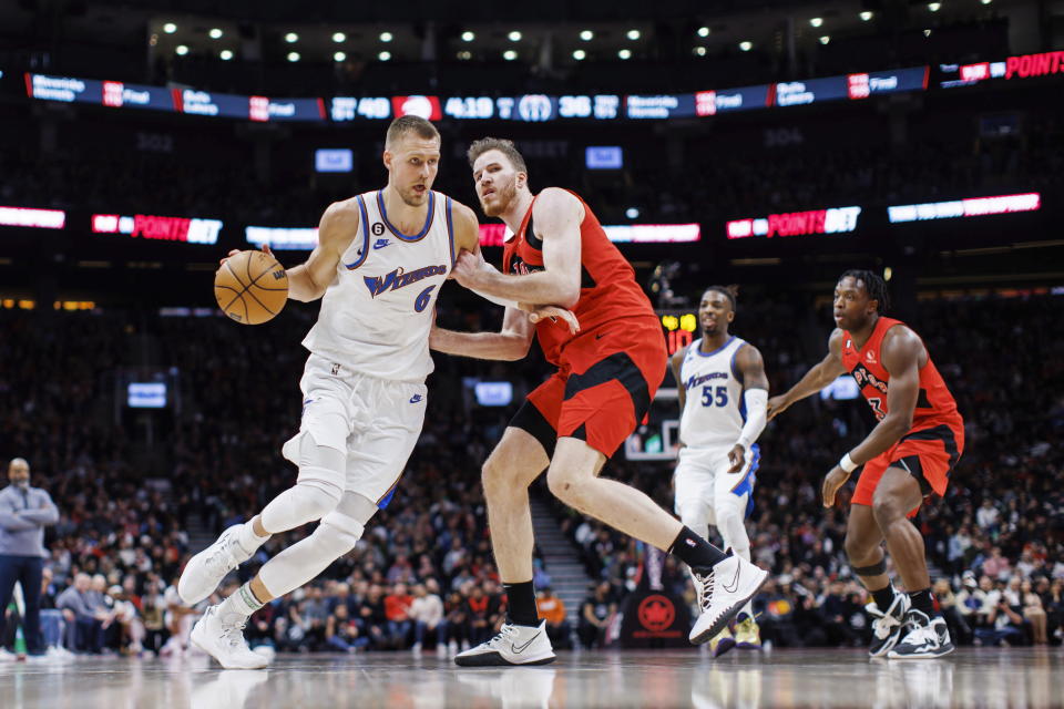 Washington Wizards center Kristaps Porzingis (6) drives to the net against Toronto Raptors center Jakob Poeltl, center, during the first half of an NBA basketball game in Toronto, Sunday, March 26, 2023. (Cole Burston/The Canadian Press via AP)