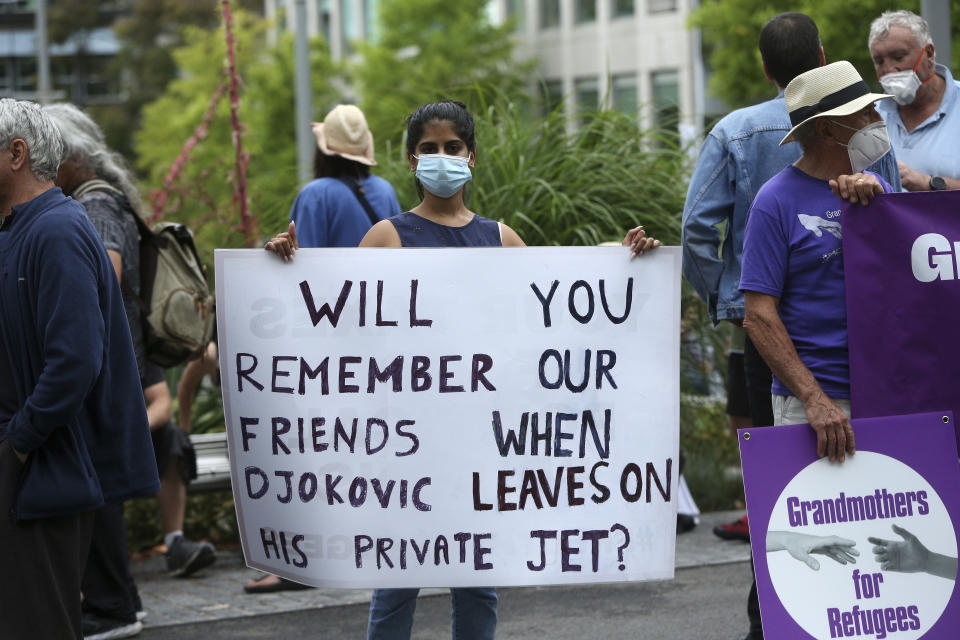 A protester hold a banner with others outside the Park Hotel calling for the release of refugees being detained inside the hotel in Melbourne, Australia, Friday, Jan. 7, 2022. The world’s No. 1-ranked tennis player Novak Djokovic is also being held there after border officials canceled his visa last week over a vaccine requirement. (AP Photo/Hamish Blair)