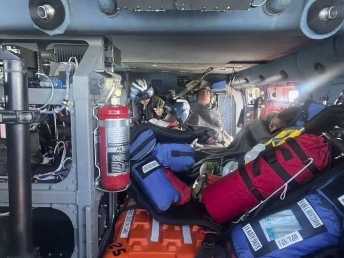 In this image provided by the U.S. Coast Guard, a Coast Guard Air Station New Orleans MH-60 Jayhawk aircrew treats three rescued boaters for injuries Sunday, Oct. 9, 2022, approximately 25 miles offshore from Empire, La. Three men whose fishing boat sank in the Gulf of Mexico off the Louisiana coast were rescued after surviving for more than a day despite being attacked by sharks that inflicted deep cuts on their hands and shredded one of their life jackets, according to their rescuers. (U.S. Coast Guard via AP)