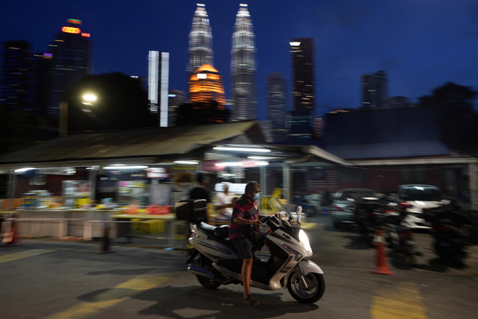 A motorcyclist wears a face mask with the background of Twin Towers in downtown Kuala Lumpur, Malaysia, Monday, Jan. 11, 2021. Prime Minister Muhyiddin Yassin says Malaysia's health care system is at a breaking point as he announced new movement curbs, including near-lockdown in Kuala Lumpur and several high-risk states to rein in a spike in coronavirus cases.(AP Photo/Vincent Thian)