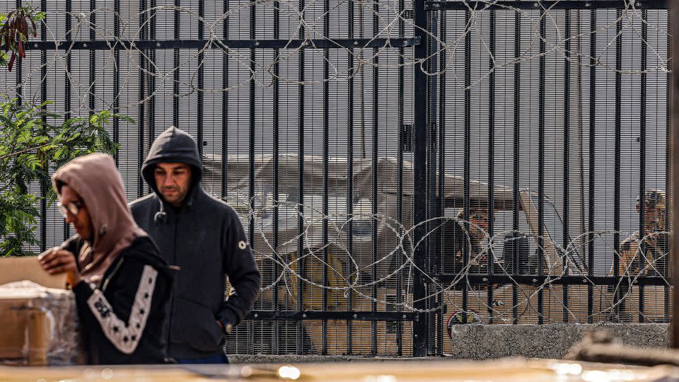 Egyptian army soldiers look on from behind the barbed-wire border fence as Palestinian workers unload crates of humanitarian aid entering the Gaza Strip through the Kerem Shalom (Karm Abu Salem) border crossing in the southern part of the enclave on January 29. - Said Khatib/AFP/Getty Images