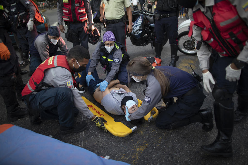 Wearing masks as a precaution against the new coronavirus, Angels of the Road volunteer paramedics, in grey and blue uniforms, place a motorcycle accident victim onto a scoop stretcher, in Caracas, Venezuela, Monday, Feb. 8, 2021. According to the volunteers, most of their calls involve traffic accidents. (AP Photo/Ariana Cubillos)