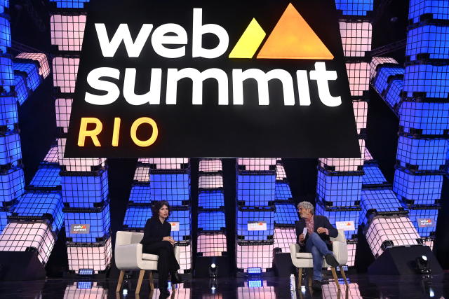 Whittaker and Michael Isikoff sit on white chairs onstage below sign reading: Web summit Rio