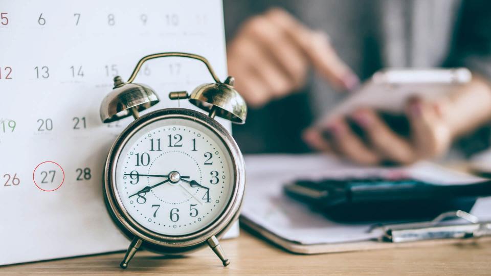 due date calendar and alarm clock with blur business woman hand calculating  monthly expenses during tax season.