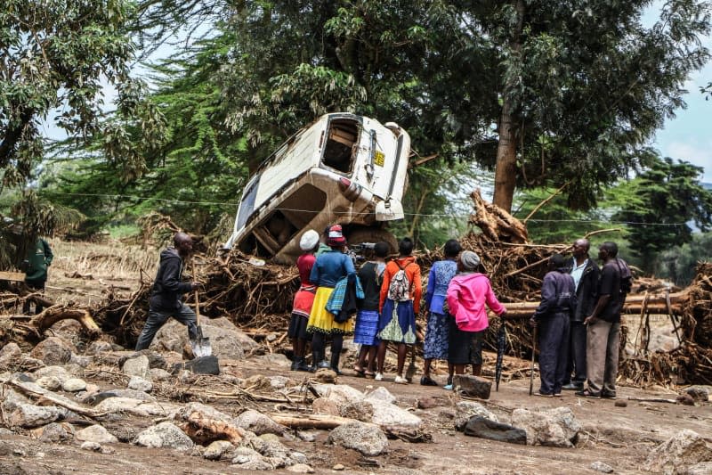 People gather beside a damaged car tossed over the debris by raging waters. Search and rescue operations are ongoing following a flooding tragedy in Mai Mahiu in Nakuru. Over 50 people have been reported dead. James Wakibia/SOPA Images via ZUMA Press Wire/dpa