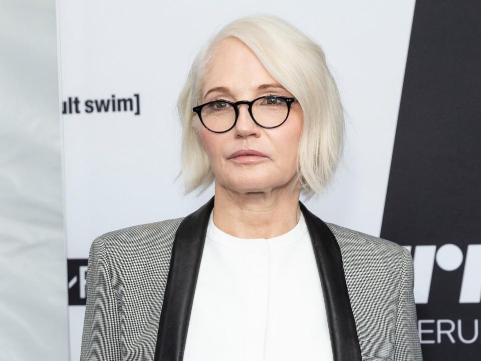 Ellen posing in in a blazer and glasses in front of a backdrop.