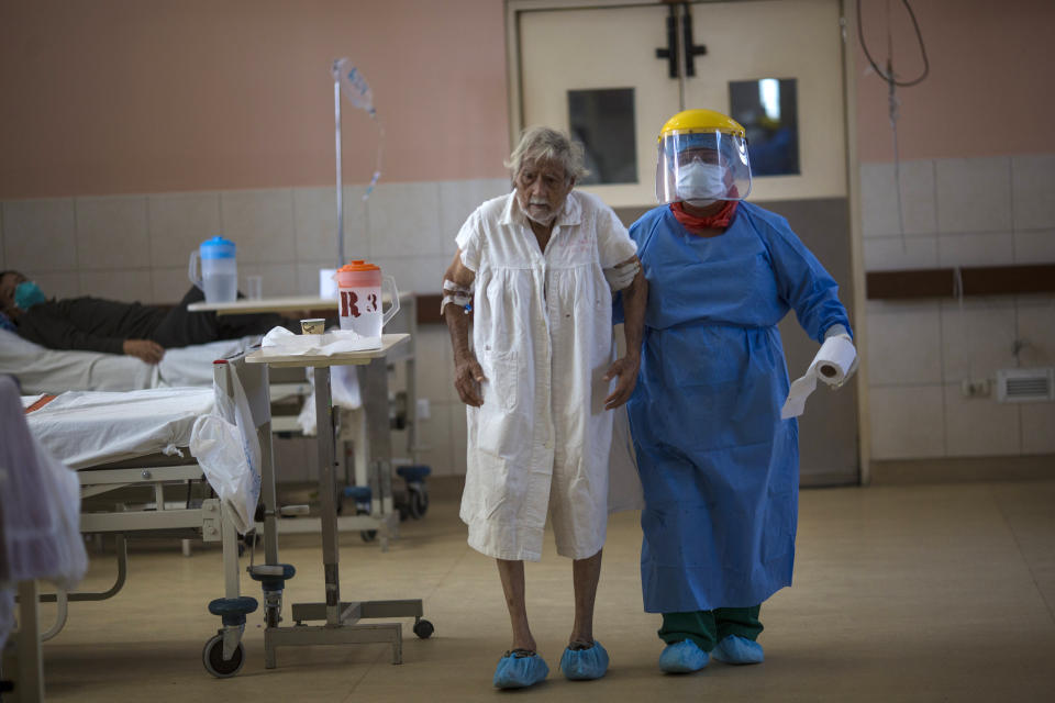 A nurse, wearing protective gear, walks with a patient inside the intensive care unit for people infected with the new coronavirus, at the 2 de Mayo Hospital, in Lima, Peru, Friday, April 17, 2020. (AP Photo/Rodrigo Abd)