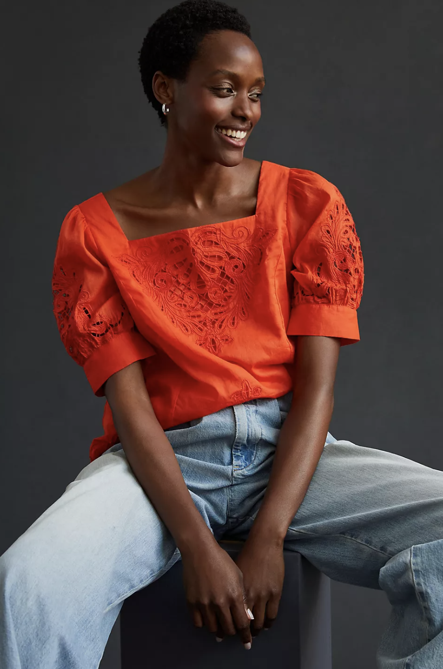 model wearing blue jeans and orange-red blouse, By Anthropologie Short-Sleeve Cutwork Blouse (Photo via Anthropologie)