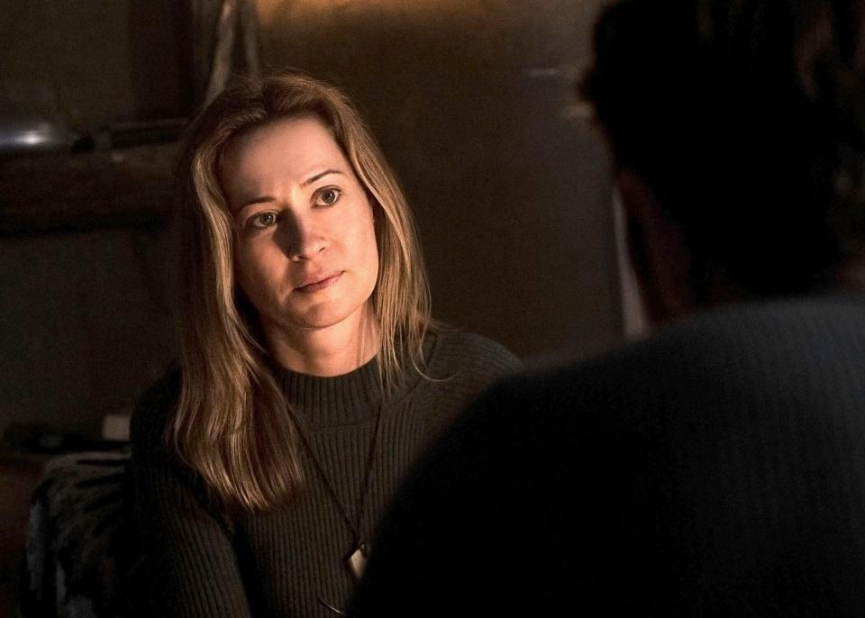 A concerned woman is illuminated by a fireplace in a cabin