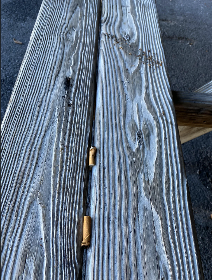 Close-up of a weathered wooden bench with two cigarette butts wedged in a crack