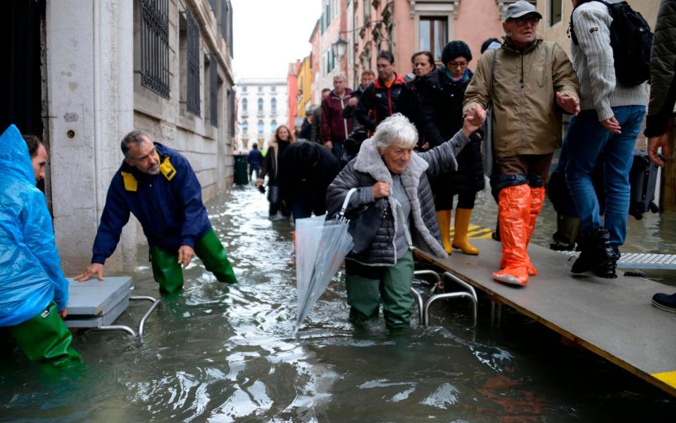 People walk on a trestle platform to try to avoid the flooding in Venice  - Andrea Merola/Ansa