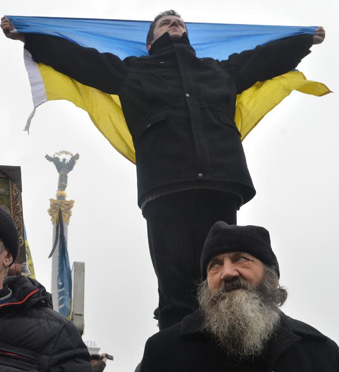 An Orthodox priest stands by an activist holding an Ukrainian flag during a mass rally of the opposition, on Independence Square in Kiev, on February 9, 2014