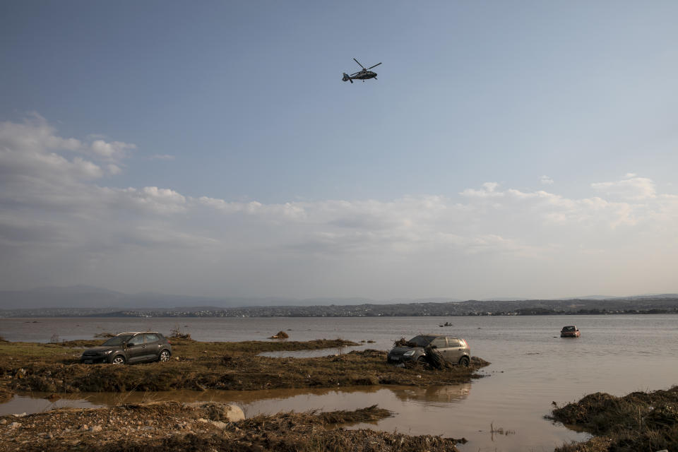 A helicopter flies over vehicles abandoned in the sea following a storm at the village of Bourtzi, on Evia island, northeast of Athens, on Sunday, Aug. 9, 2020. Five people, including en elderly couple and an 8-month-old baby have been found dead, two more are missing and dozens have been trapped in their homes and cars as a storm hits the island of Evia in central Greece, authorities said Sunday. (AP Photo/Yorgos Karahalis)